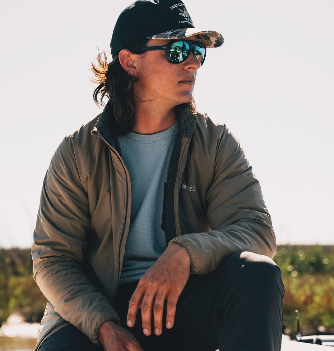 An angler sits on a boat while wearing a lightweight jacket. 