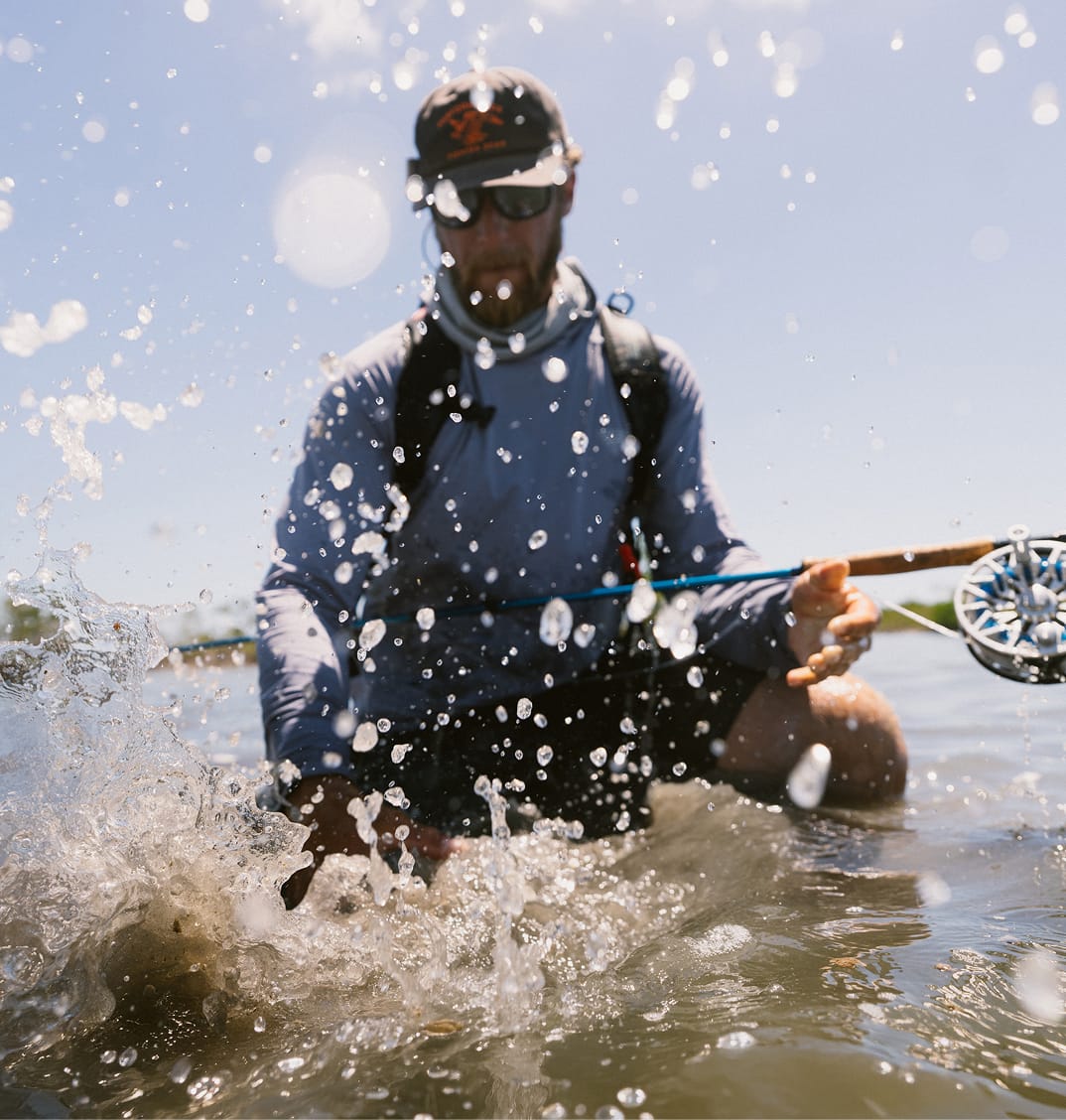 An angler crouching down in water grabbing a fish. 