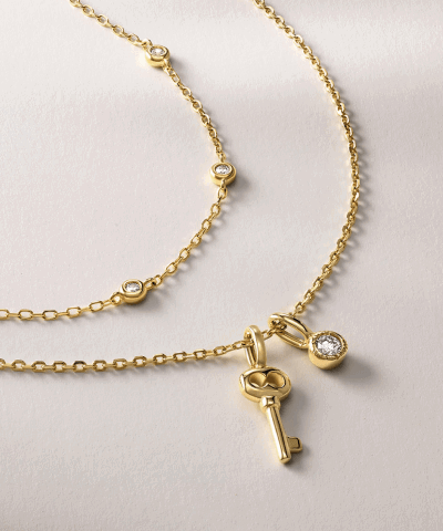 Yellow gold necklaces featuring bezel-set round clear stones, a key charm and a bezel-set oval pendant.