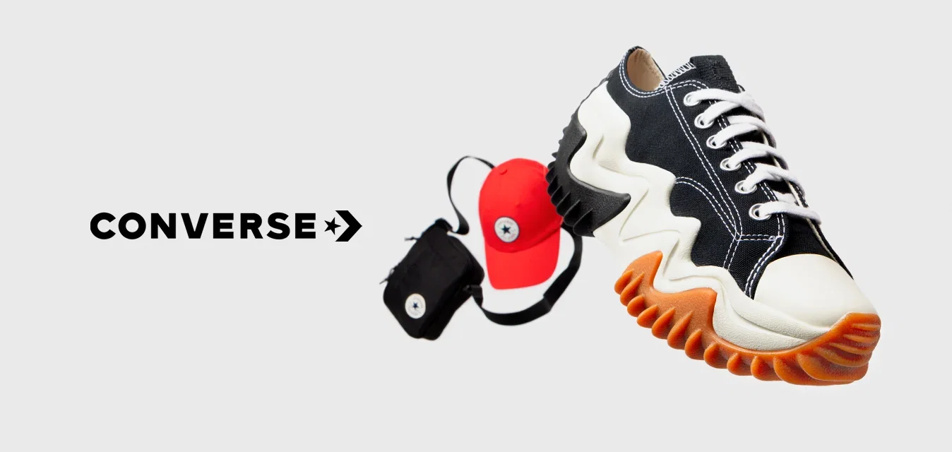 Zwart-witte sneaker met zigzagzool en oranje accenten, naast een rode pet en een kleine zwarte tas met een circulair logo.