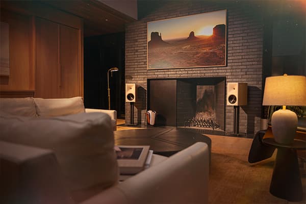 Pair of red oak Klipsch Sevens II speaker, on black stands, in a dimly lit living room, situated by a fireplace.