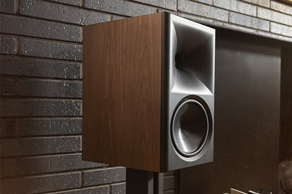 Pair of walnut Klipsch Nines II speaker, on black stands, situated by a fireplace.