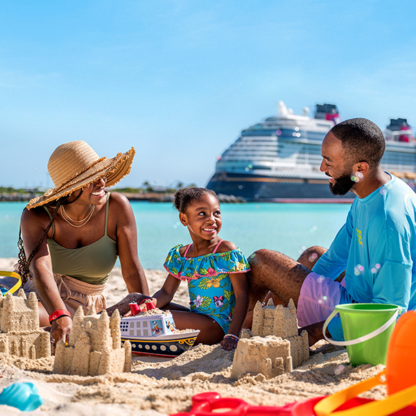 A family builds sandcastles on the beach of Disney Castaway Cay as the Disney Cruise Line ship floats in the background.