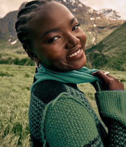 Woman wearing a green knit jumper and scarf in a mountain landscape.