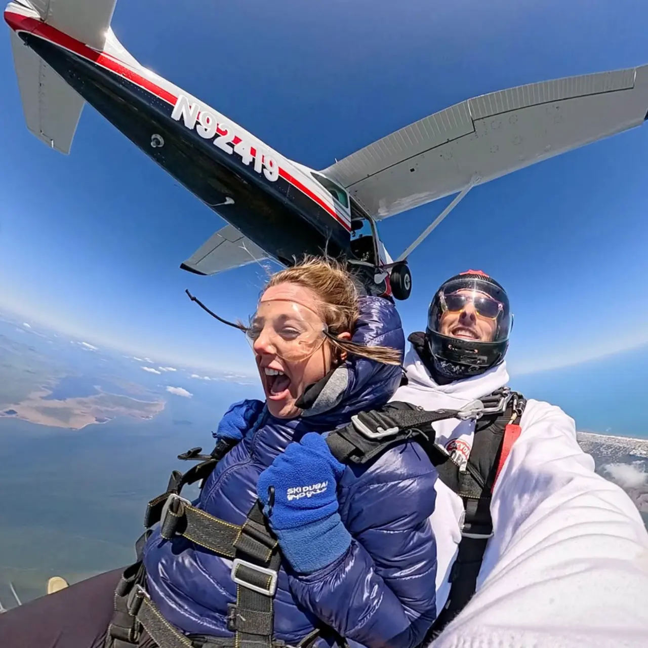 A tandem skydiver and a client captured mid-air with an airplane in the background.