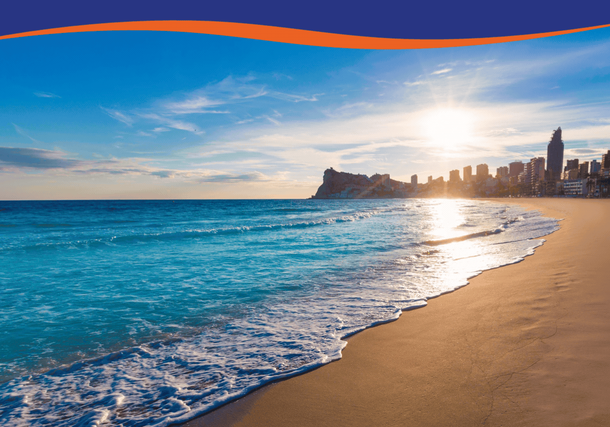 Sunset over a beach with gentle waves and a city skyline in the background.