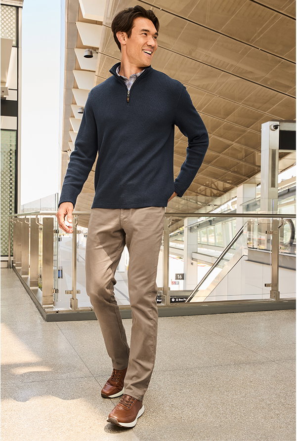 Model wearing a navy quarter-zip, tan pants, and brown Douglas sneakers while walking through a transit station.