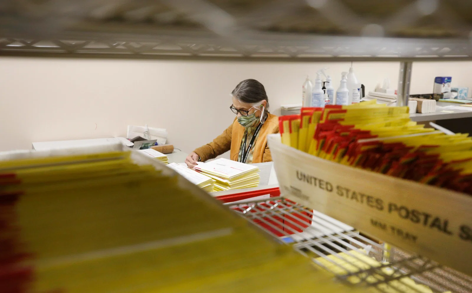 A postal worker sorts through trays and stacks of mail-in ballots.