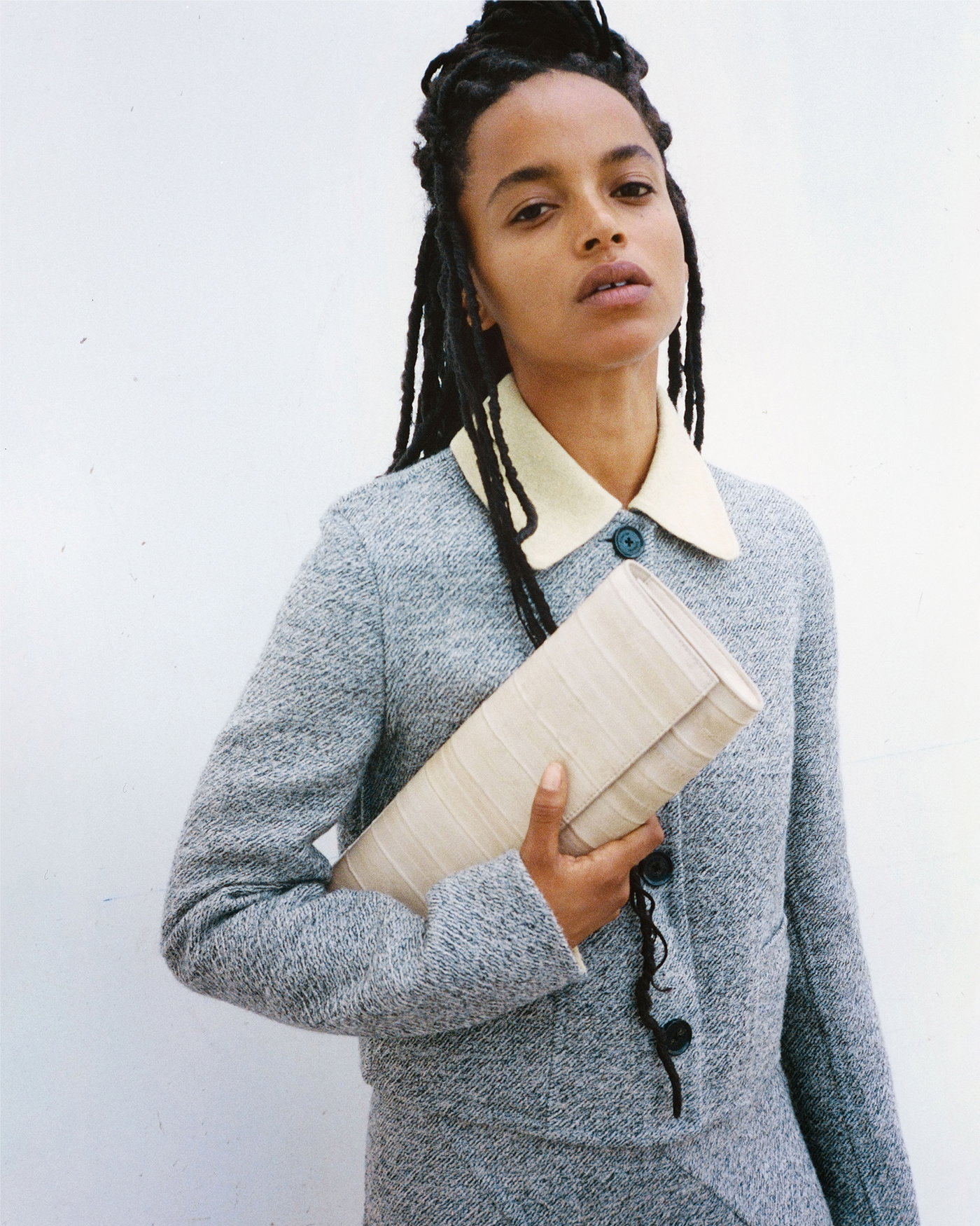 Cropped Campaign Image of model wearing the Gaelle Jacket in Double Face Melange Outerwear in Ecru Tahini Multi with the Gaelle Skirt in Double Face Melange Outerwear in Ecru Tahini Multi, holding the Hex Clutch in Eel in Ivory