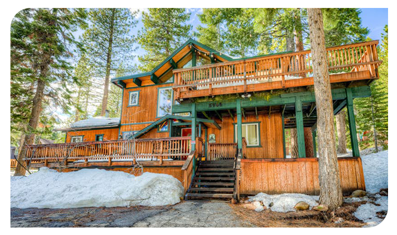 Rustic forest cabin surrounded by tall pines and patches of snow.