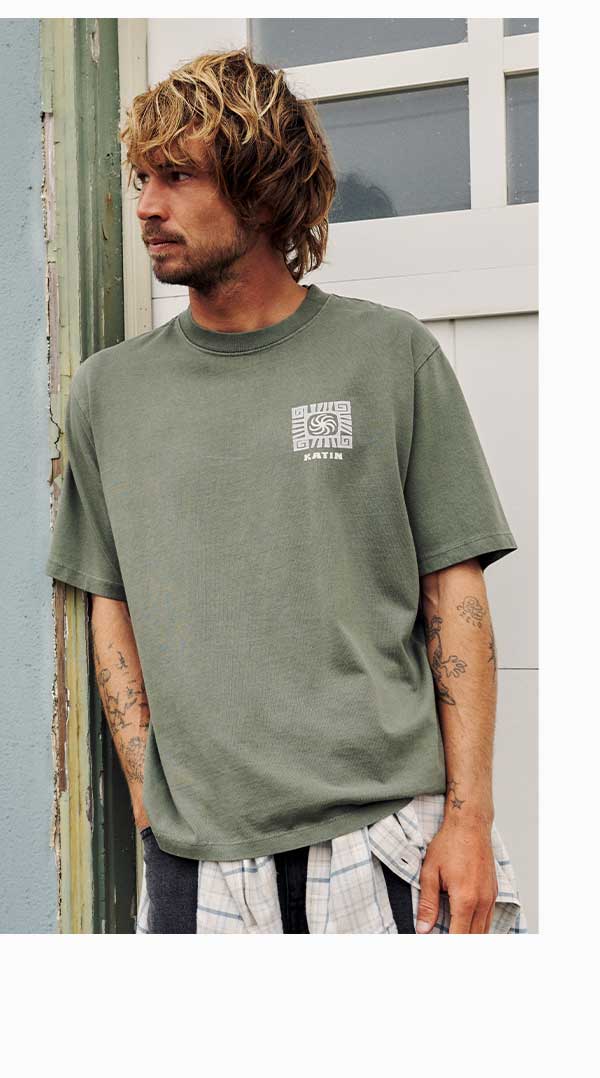 Man wearing an olive green Katin graphic t-shirt standing in a doorway
