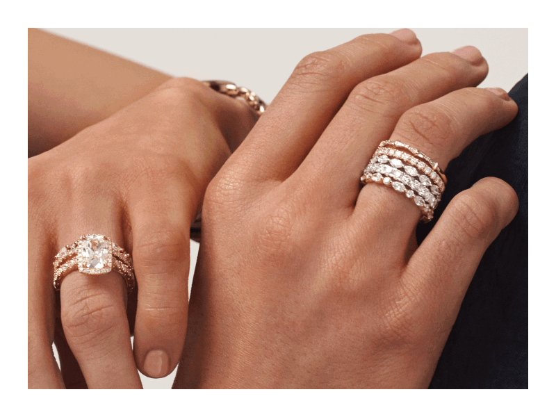 Hands displaying a diamond engagement ring and stacked diamond bands in yellow and white gold.