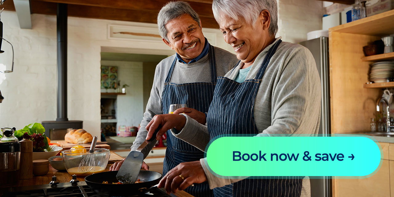 A man and woman cooking their dinner on a stove while laughing