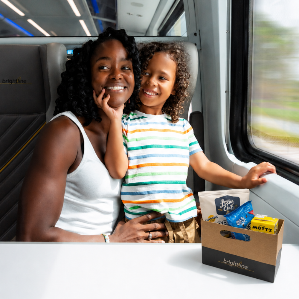 A mother and son smiling on the train with a snack box in front of them.