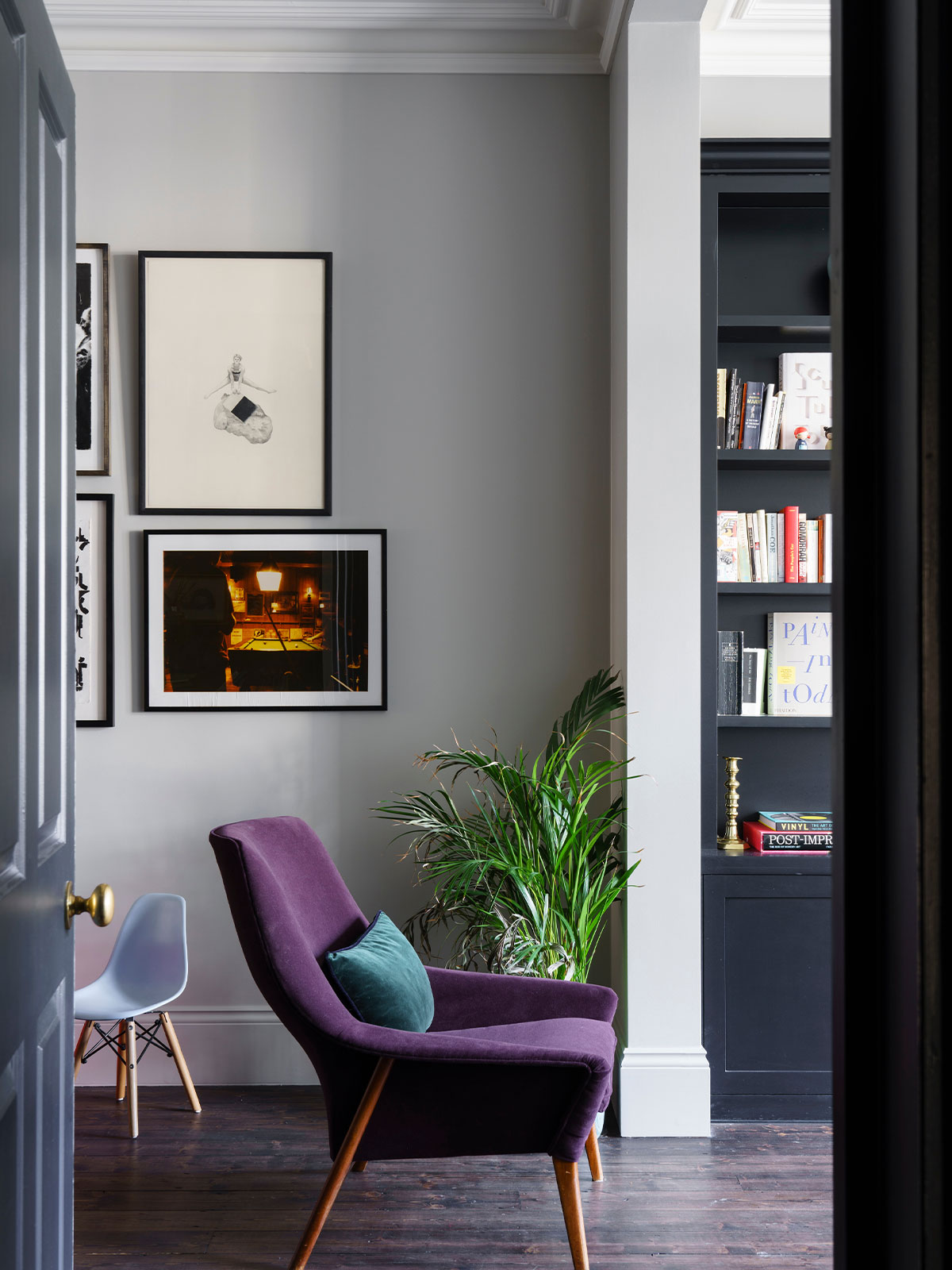 Modern reading nook with a purple armchair, teal cushion, framed art and indoor plant.