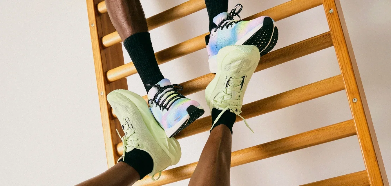 Twee mensen in sportschoenen en zwarte sokken interactief met een houten wandladder tegen een eenvoudige witte muur.