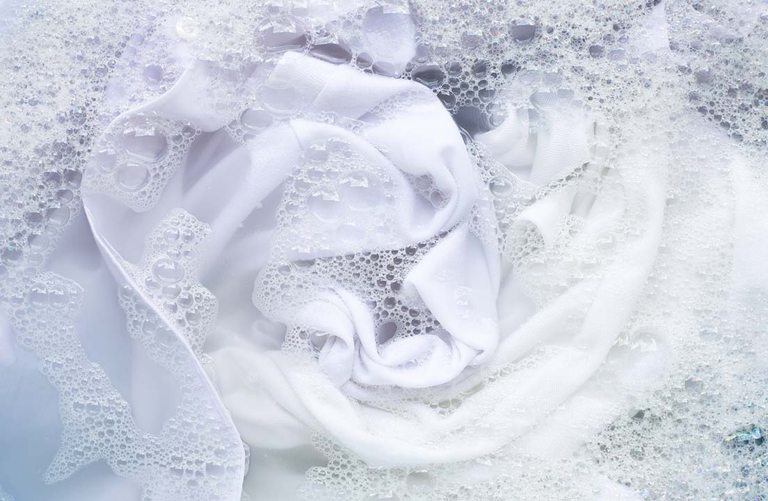 White clothes surrounded by detergent suds inside a washing machine