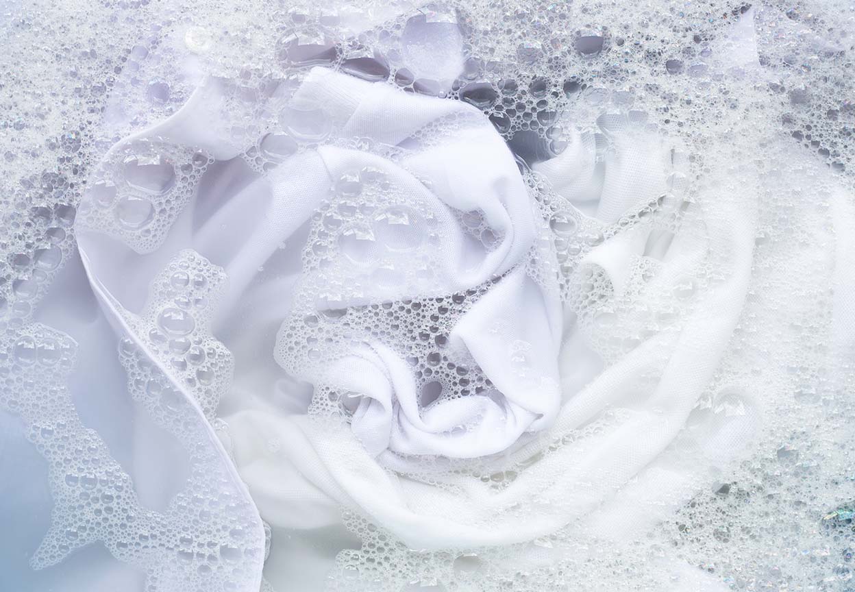 White clothes surrounded by detergent suds inside a washing machine