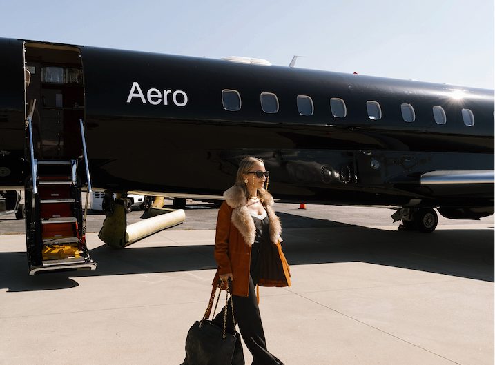 Nicole Richie dressed in a cognac brown coat with fur trim walks away from a black Aero jet on the tarmac.