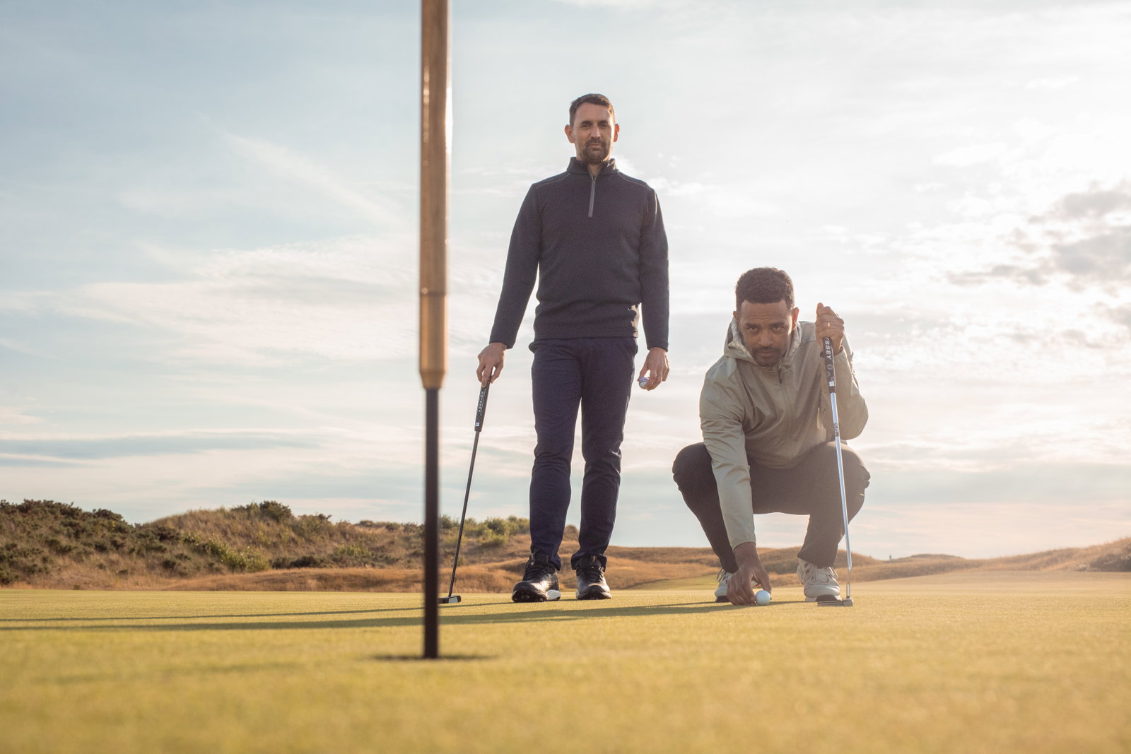 Golfer lining his ball up for a putt whilst his playing partner watches on