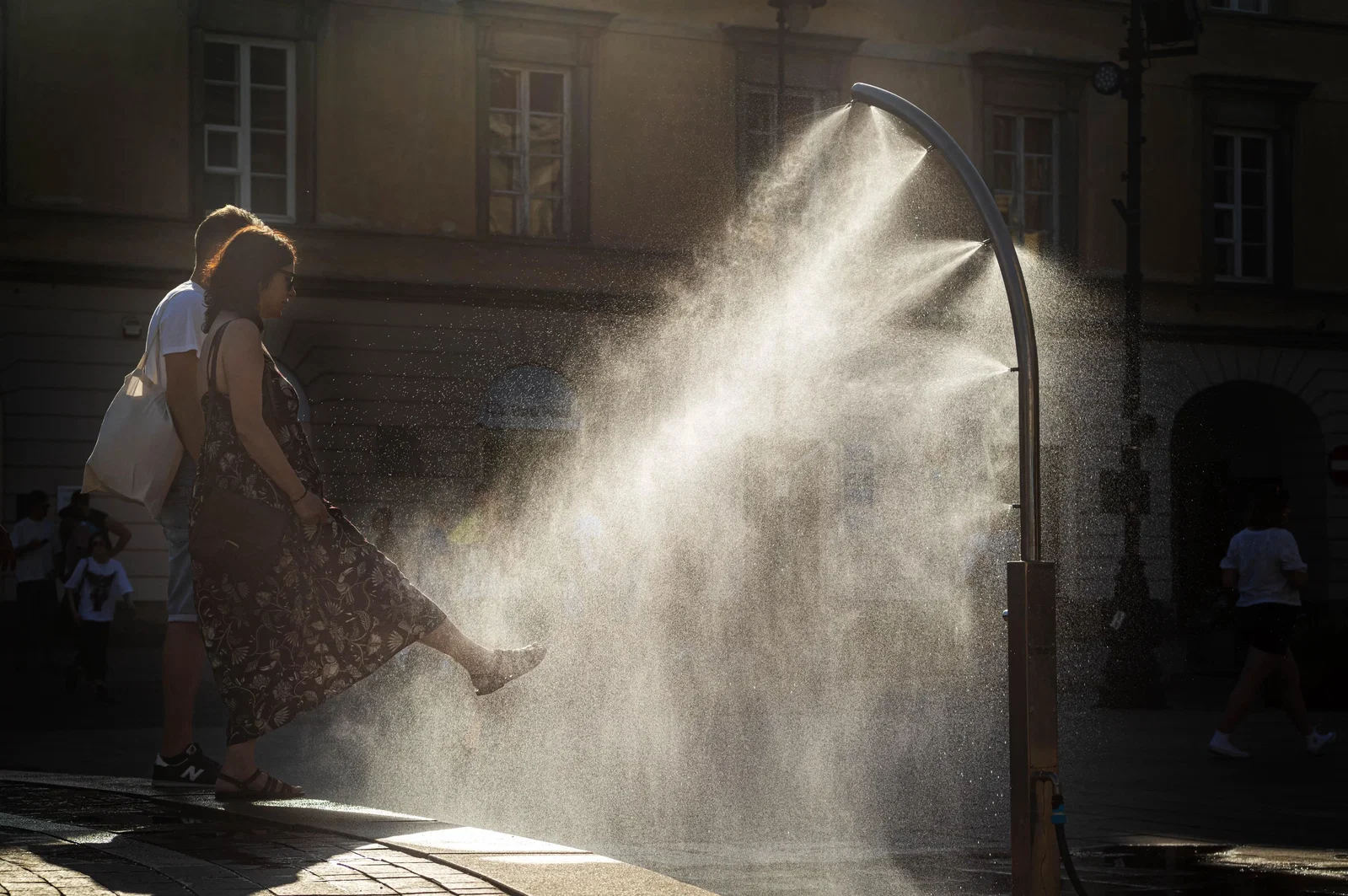 Two people stand near a public cooling station that is spraying water at night, lit by a streetlight.