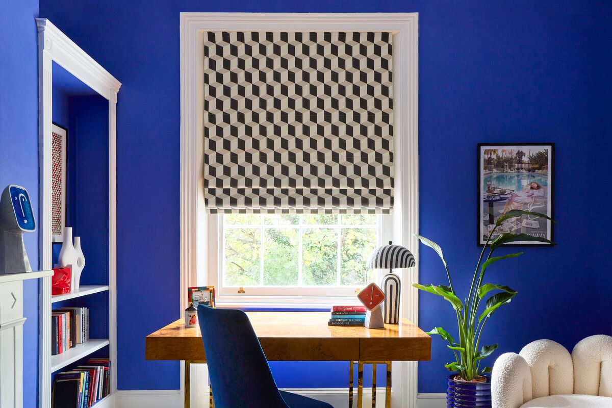 Geometric grey and cream Roman blind at a window, creating a bold focal point in a vibrant blue home office with a wooden desk.