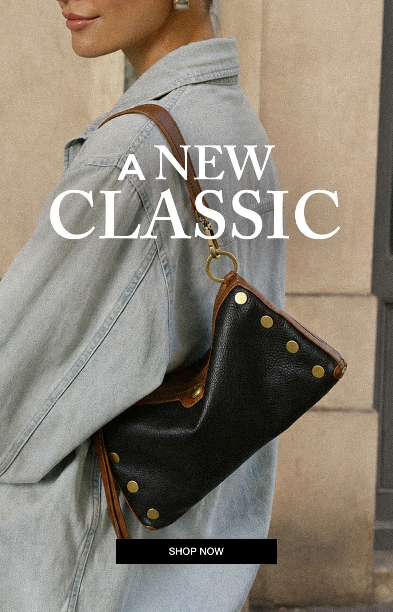 A NEW CLASSIC. Model in a light-wash denim jacket carrying an East End black leather bag with rich brown trim and gold hardware. SHOP NOW.