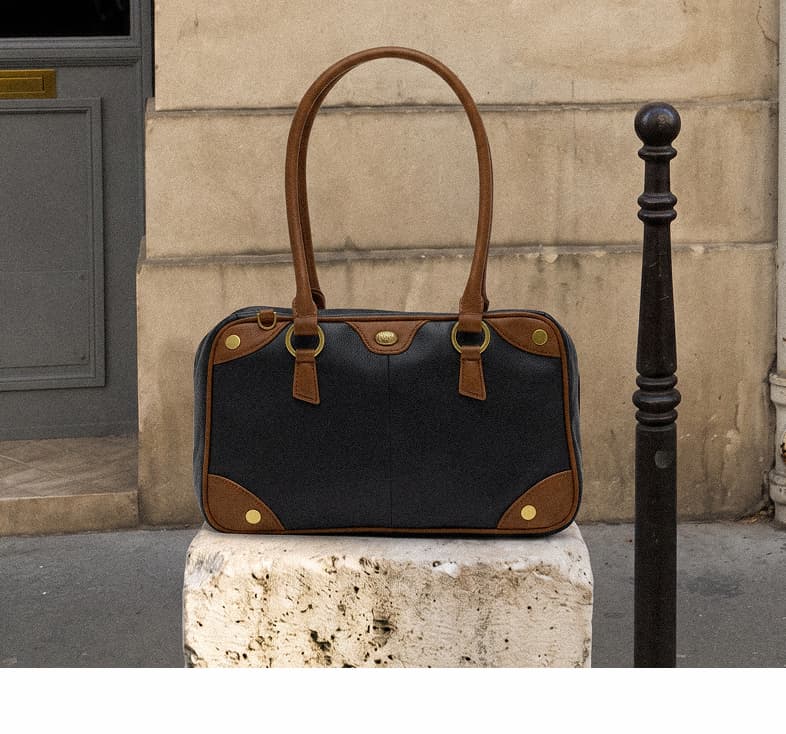 East End Meredith Lrg,  black leather handbag with rich brown trim, long top handles, and gold hardware displayed on a city sidewalk.
