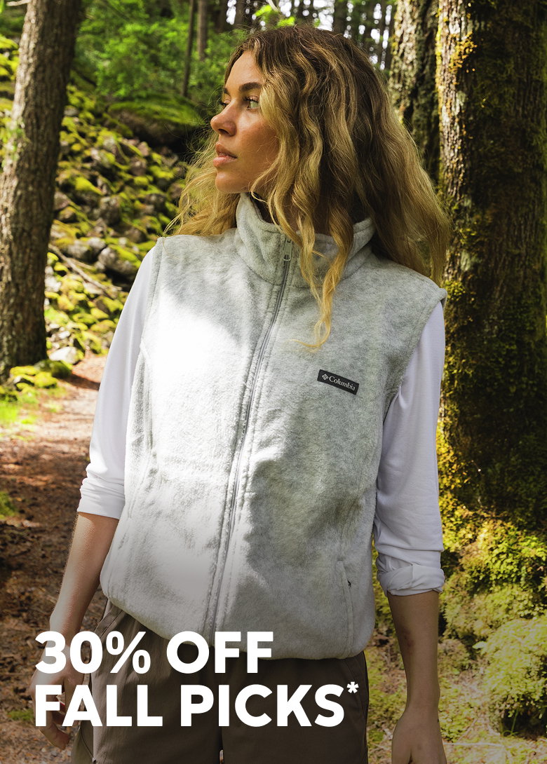 A woman standing outside, wearing a white shirt and vest with text: 30% OFF FALL PICKS*