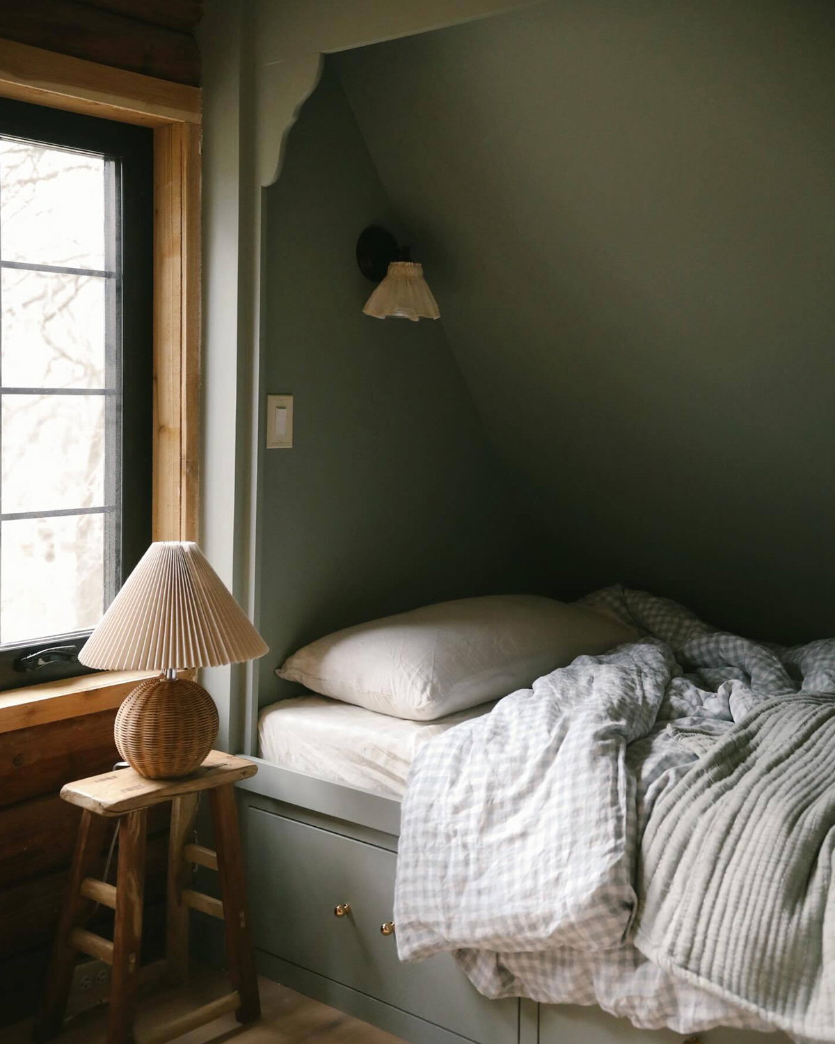 Cosy children's bedroom in Farrow & Ball Pigeon, with a built-in bed tucked beneath a sloping wall, layered neutral bedding and a wooden bedside stool with a pleated lamp.