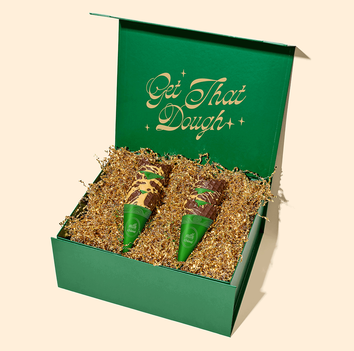 Open green gift box filled with gold crinkle paper and two chocolate-dipped cookie dough cones in green Milk Bar x Chime sleeves.
