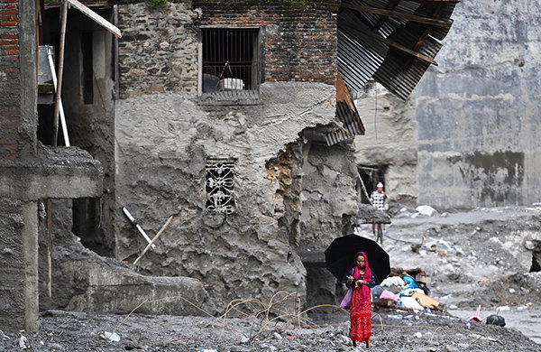 A woman wearing a red sari walks among the ruins of a flash flood.