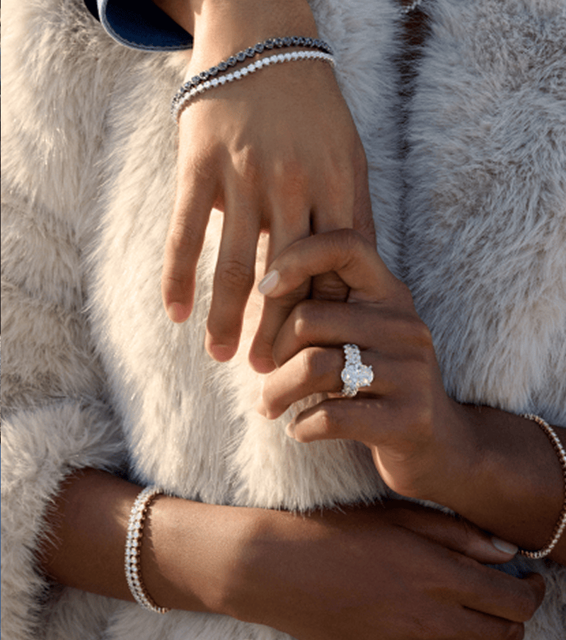 Woman in fur coat wearing diamond engagement ring and holding a hand.