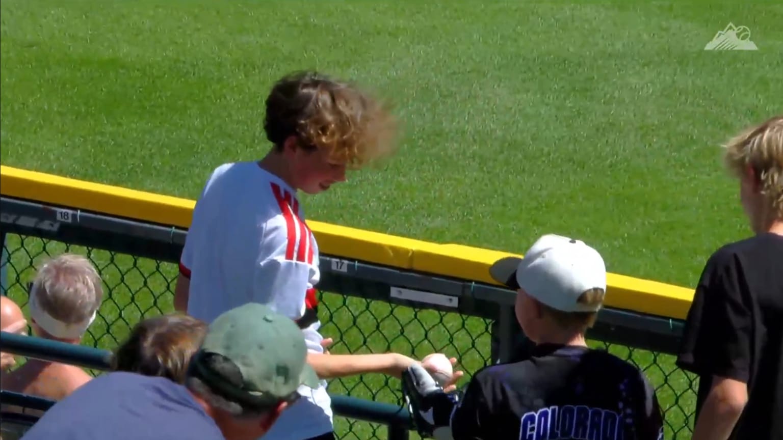 A boy at the Rockies game hands a ball to another young fan