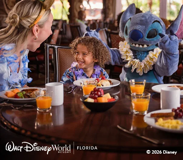 Child and parent seated at a restaurant table with a Disney character, Stitch, during a character dining experience at Walt Disney World Resort.