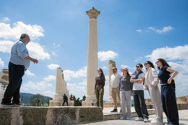 Group tour at an ancient archaeological site with towering columns and blue skies.