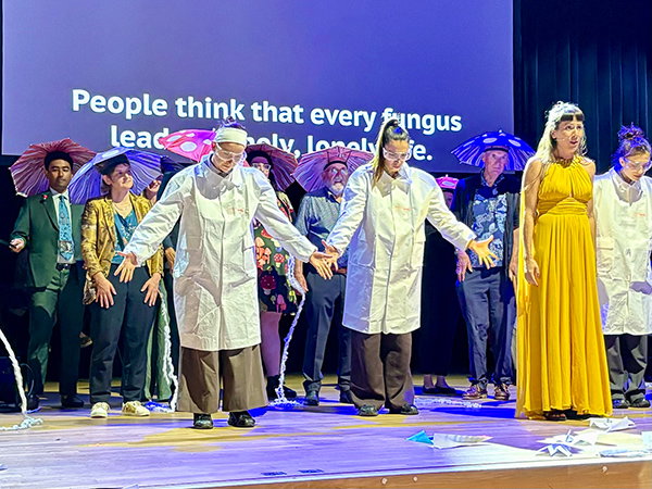 A theatrical stage performance at the Ig Nobel prize ceremony in Zurich, with Nobel laureates in the background wearing umbrella hats.