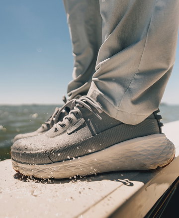 A man's gray deck shoes as he stands on a boat deck.