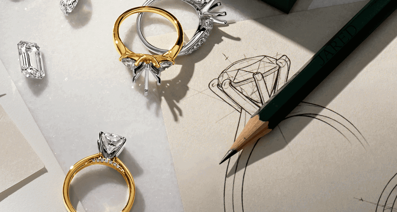 Engagement ring stones and settings next to pencil and design sketches.