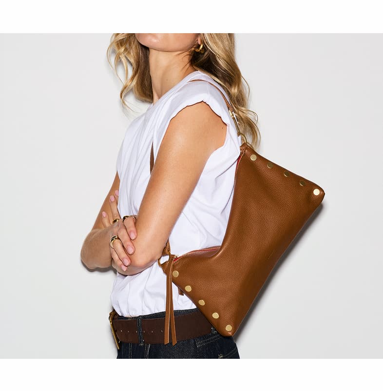 Model in a white top and jeans carrying a Kyle Med  in mahogany pebble leather shoulder bag with gold rivet details.