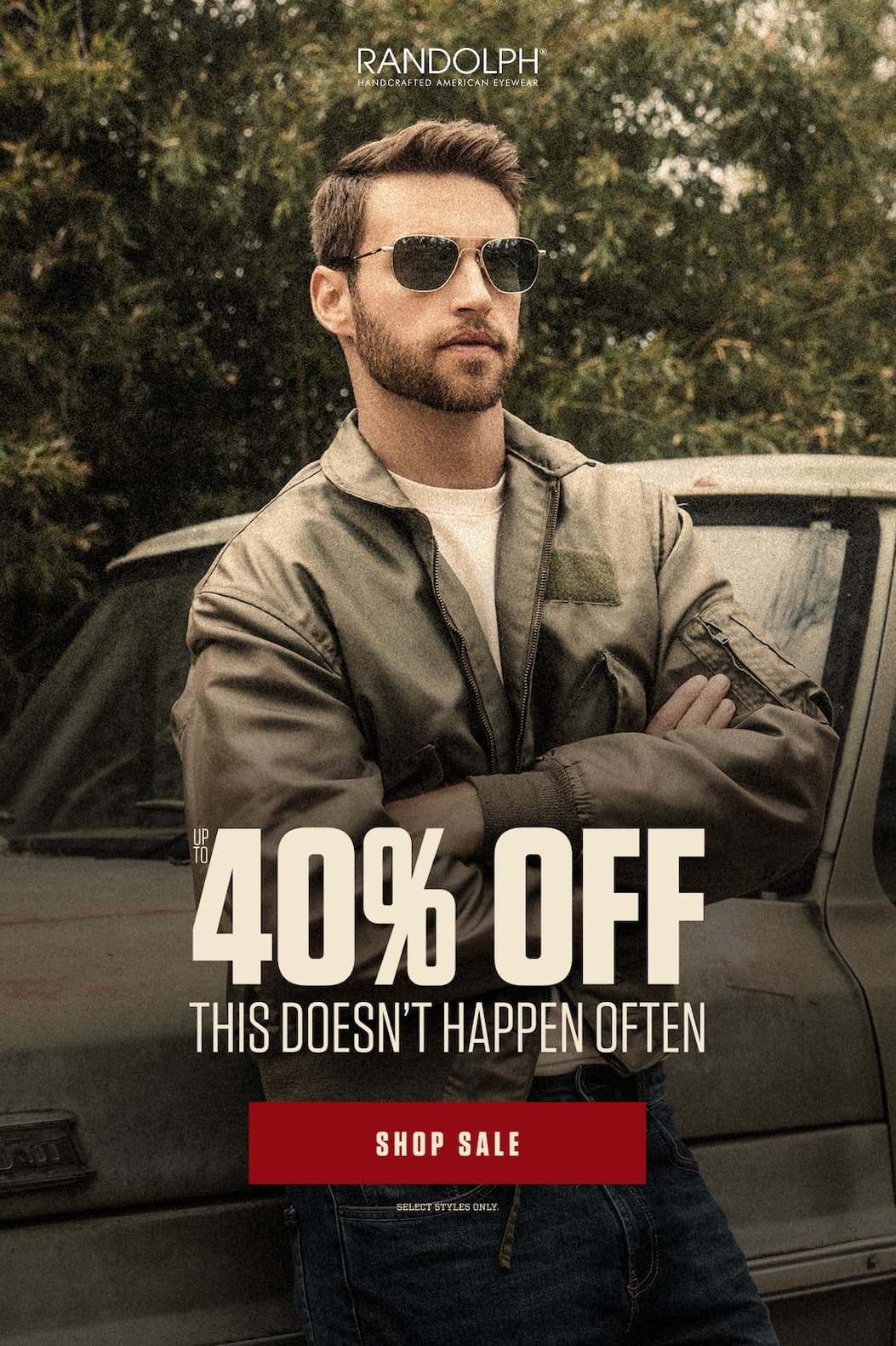 Man wearing RANDOLPH aviator sunglasses beside a vintage car.