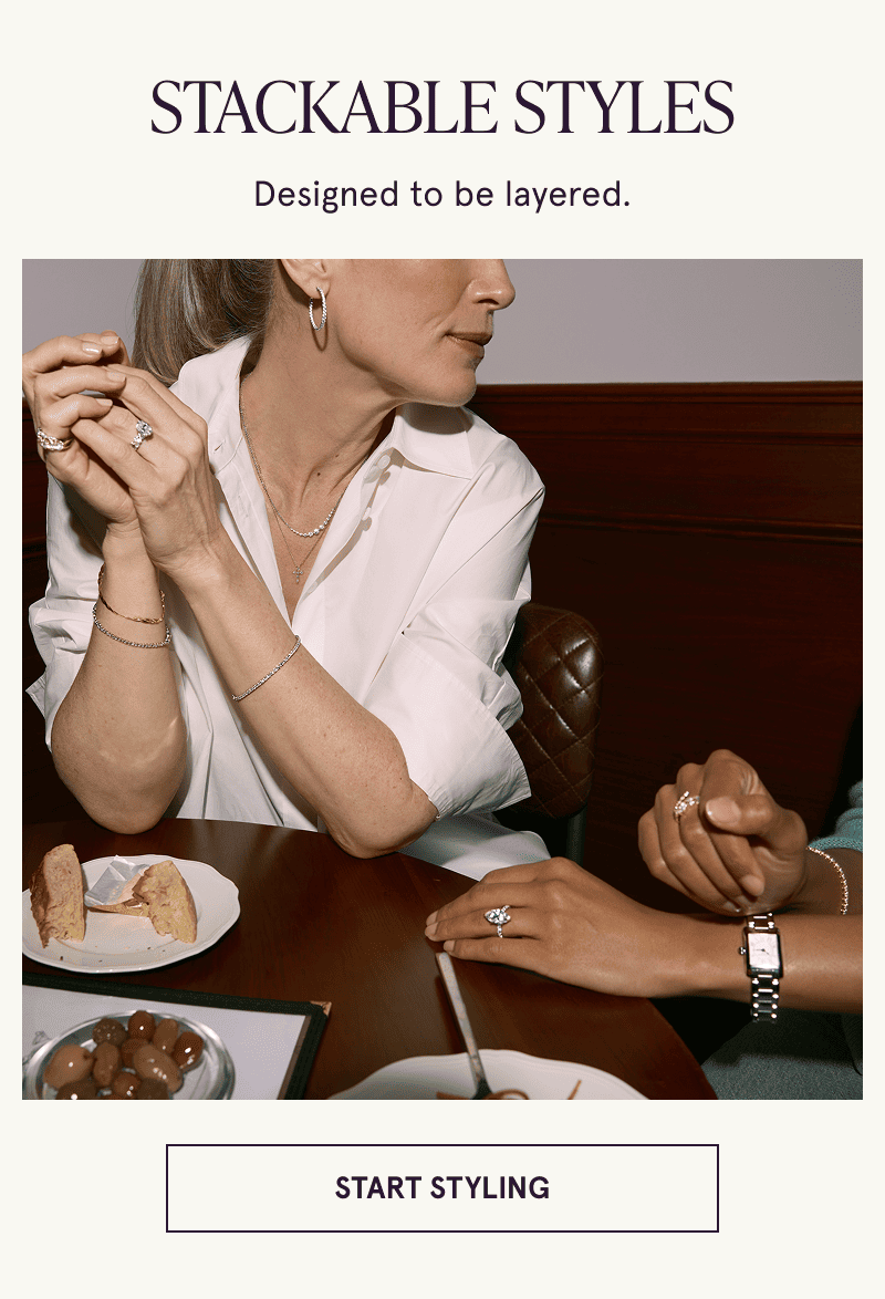 Two models wearing gold diamond jewelry sit at a table. Stackable styles. Click here to start styling