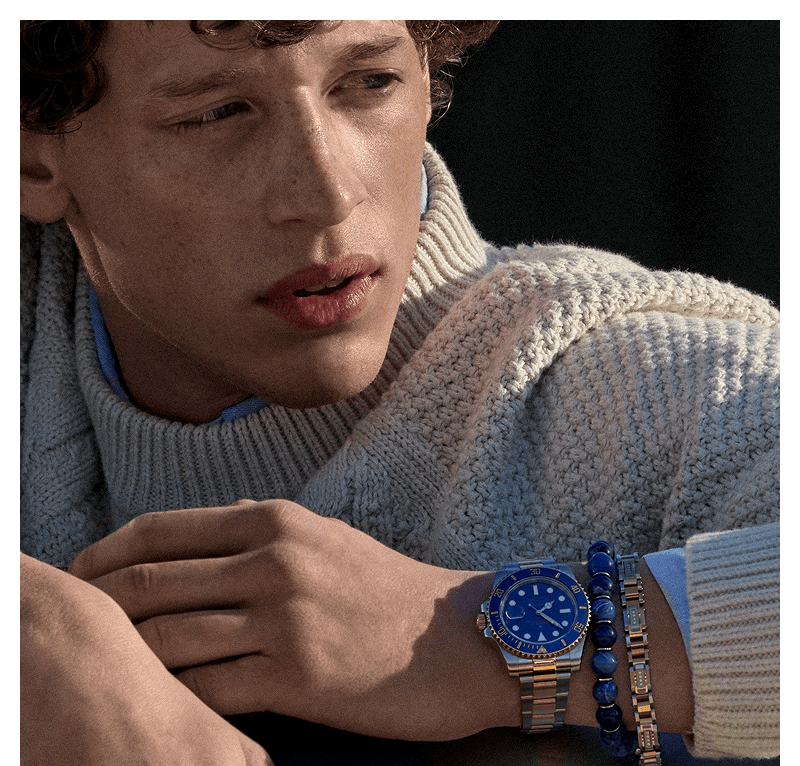Close up of male model in cable-knit sweater wearing watch and bracelets.
