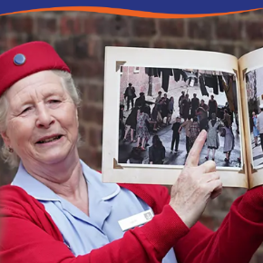 A woman in a red hat holds an open photo album, pointing at images of a crowd outdoors.