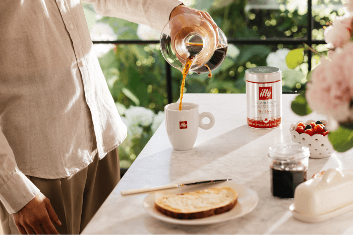 Pouring illy Classico coffee into a cup beside a breakfast setting