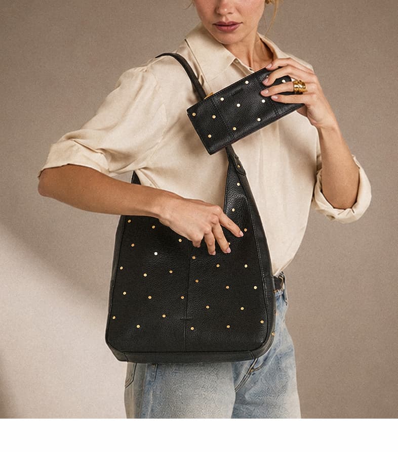 Model carrying a Tim Starlight Black leather shoulder bag with mini brushed gold rivets while holding a coordinating Starlight Black leather wallet.