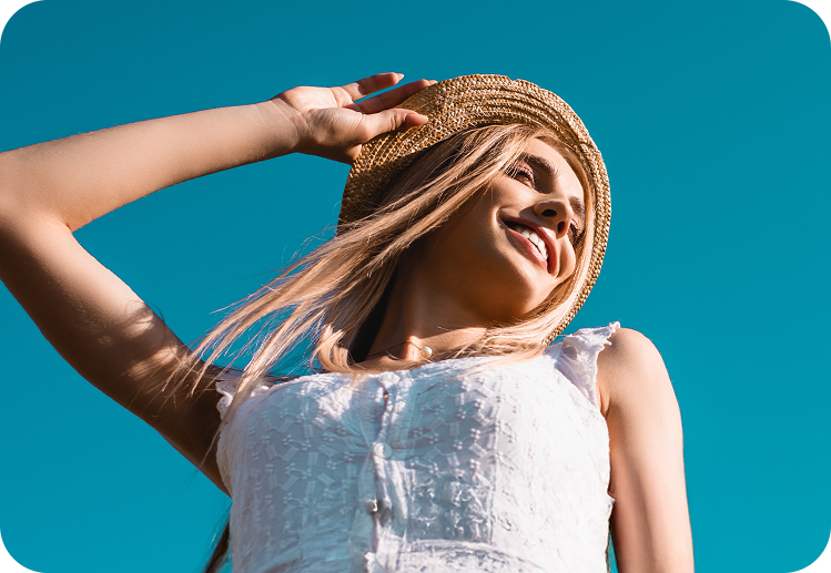 Lächelnde Frau mit Sonnenhut genießt einen sonnigen Spätsommer Tag im Freien.