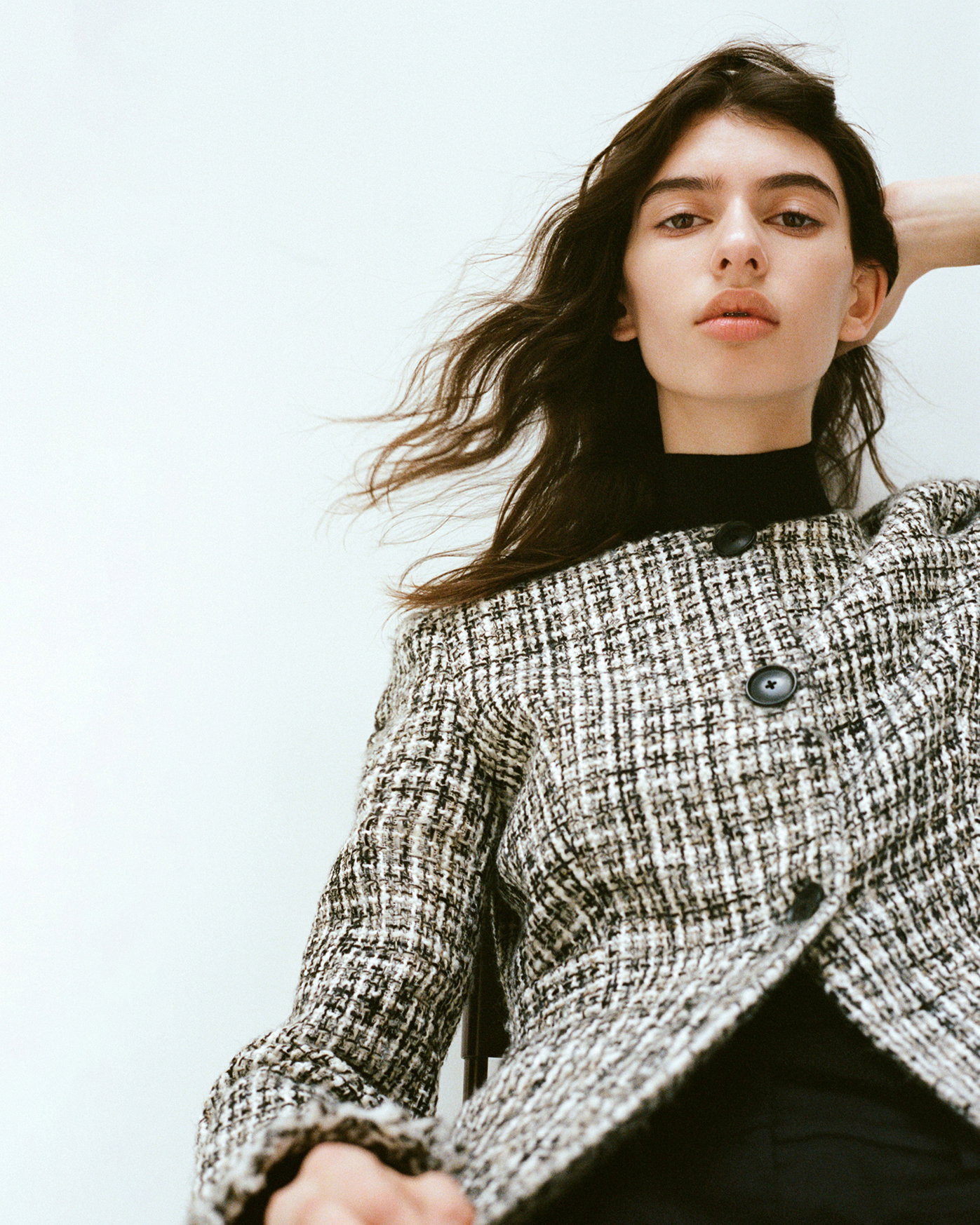 Cropped image of model sitting down wearing the Aurelia Jacket in Tweed in Black and White with her arm behind her head
