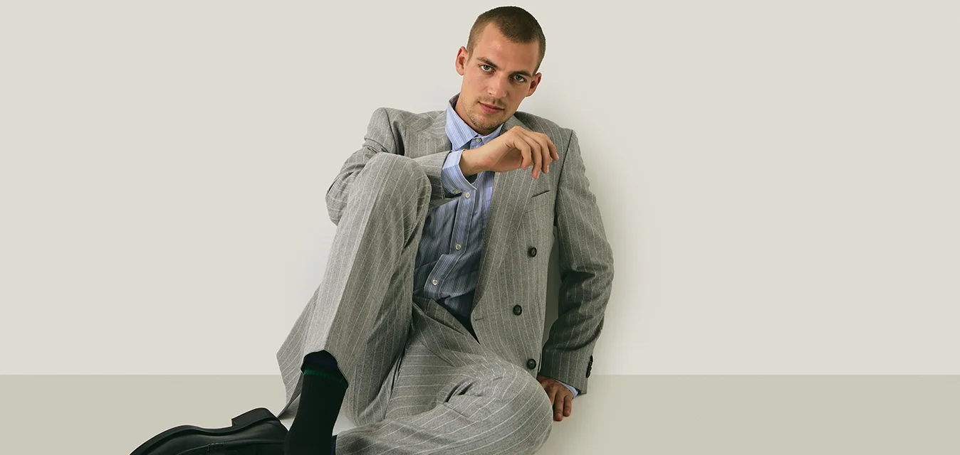 Grijze pinstriped pak met een dubbelknopen blazer en losse broek, gecombineerd met een lichtblauw gestreefd overhemd en zwarte schoenen.