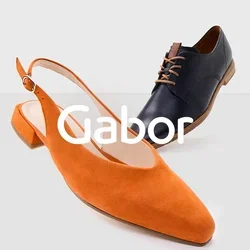 Oranje suède slingback schoen met een spitse neus en een lage hak naast een zwart leren veterschoen met een ronde neus en bruine accenten.
